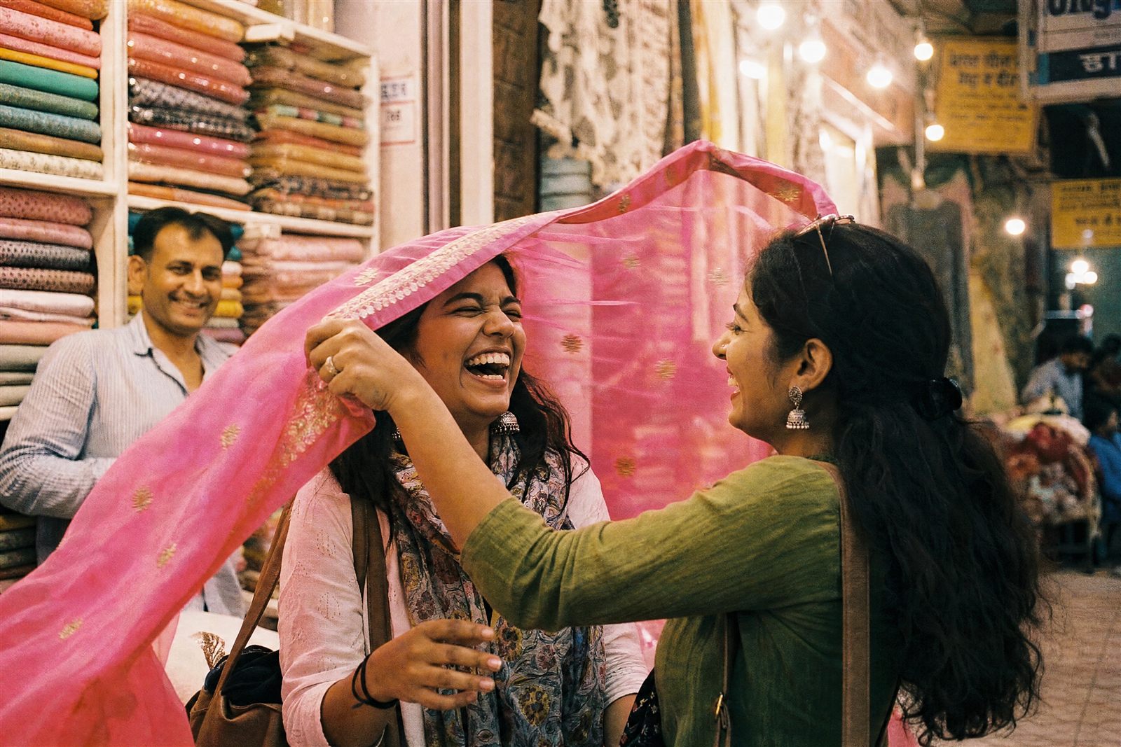 Two women laughing while shopping for dupattas in a Jaipur bazaar