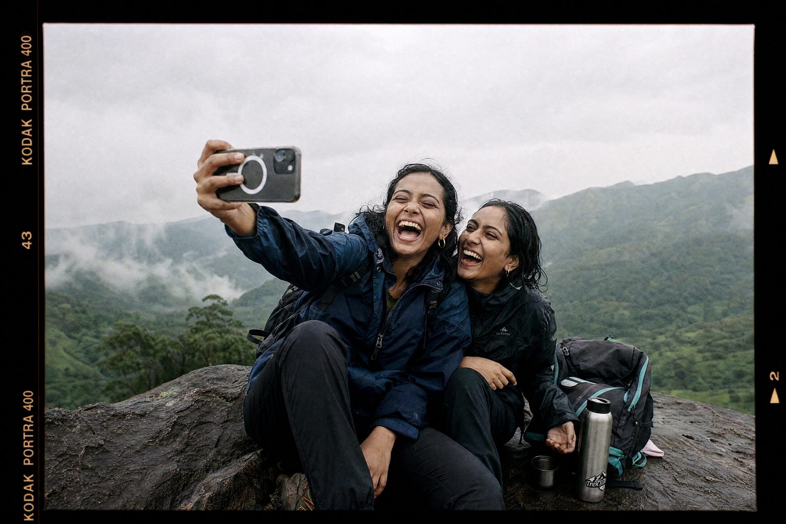 Two women taking a laughing selfie on a misty hilltop trek